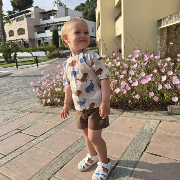 Categoria Baieti. Băiețel purtând compleu băieți bej cu balene albastre și pantaloni scurți maro.